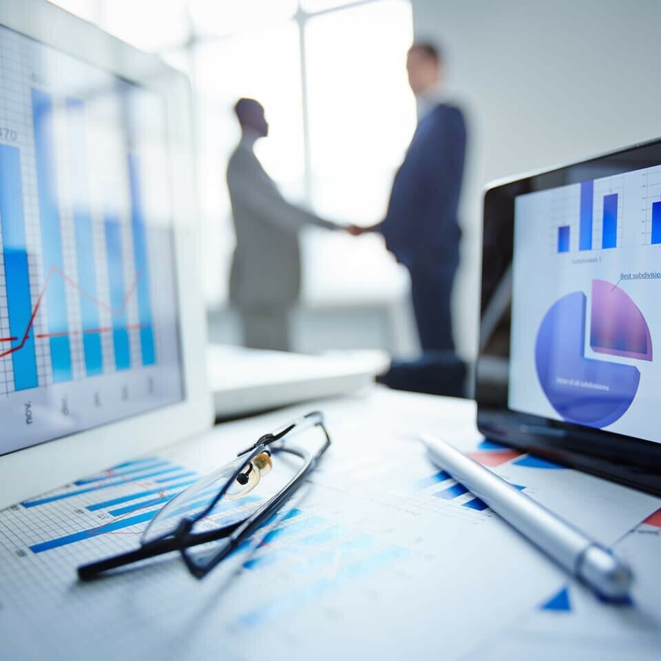 men shaking hands in the background with graphs and charts on a computer screen