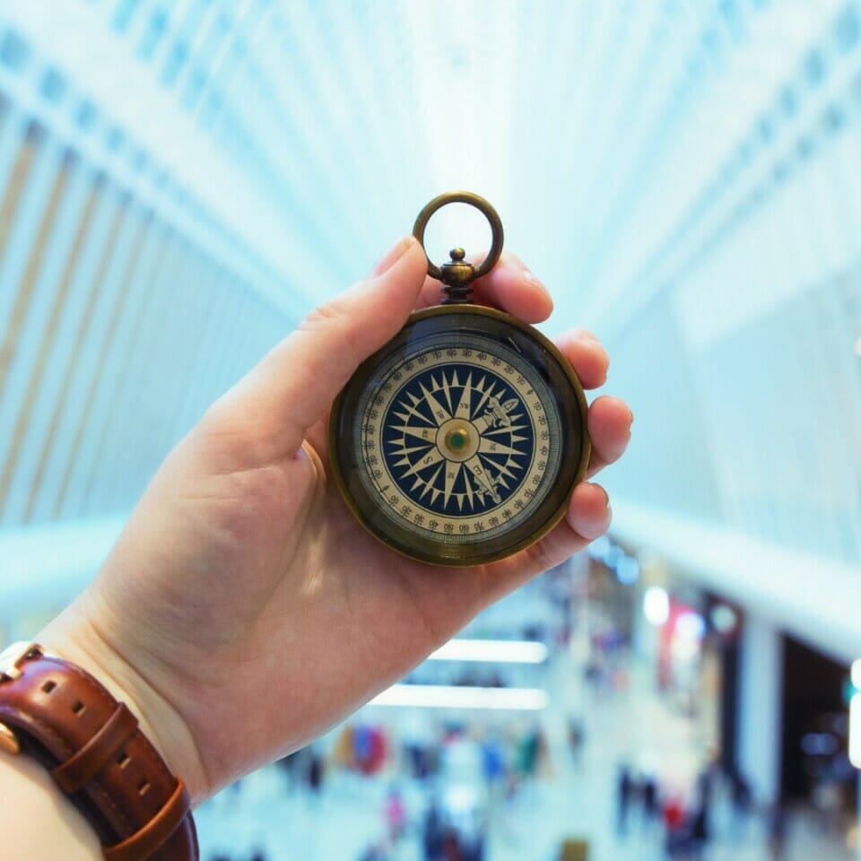 man's hand holding a compass inside a blurred background of a building concourse