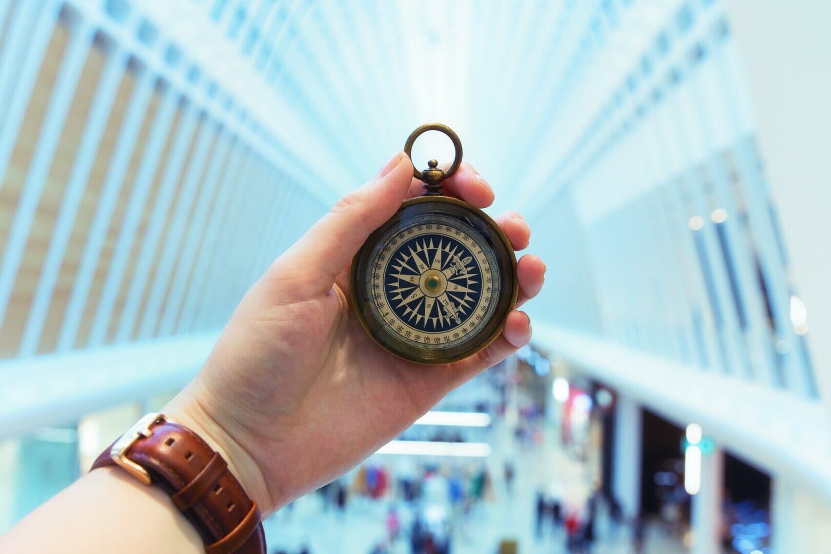 man's hand holding a compass inside a blurred background of a building concourse